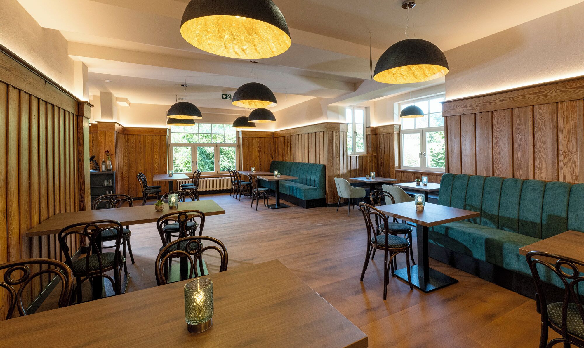 Ein Restaurant mit Holzwänden, verschiedenen Sitzbereichen, darunter Boxsitzgelegenheiten und Tische, sowie Pendelleuchten.