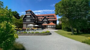 A large, multi-story building with a stone facade, a red-tiled roof, and a paved driveway leading to a seating area with umbrellas. - Wohnpark Hotel (Heppenheim)