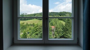 A window with a view of a green landscape, including trees and a hill. - Wohnpark Hotel (Heppenheim)