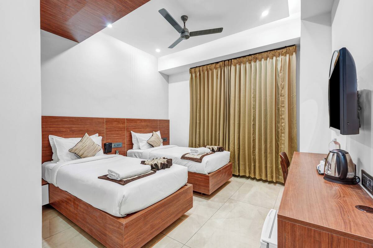 A hotel room with two beds, a desk, a television, and a ceiling fan.