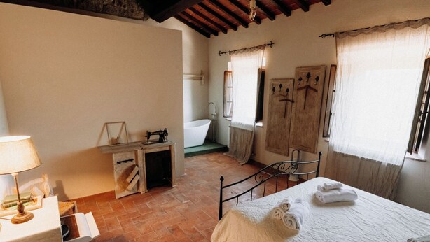 A room with a bed, a desk with a lamp, a wooden cabinet, and a window with curtains. - Vitalenta Agriboutique (Pienza)