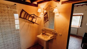 A bathroom with a tiled wall, a wooden chair leaning against the wall, a sink with a mirror, and a window. - Vitalenta Agriboutique (Pienza)