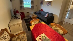 En kompakt opholdsstue med sofa, et lille spisebord, et skrivebord med computer og en rød stol.