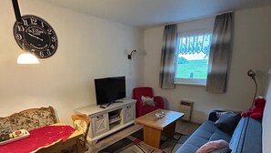En stue med sofa, fjernsyn, rød lænestol, spisebord med stole og et ur på væggen.
