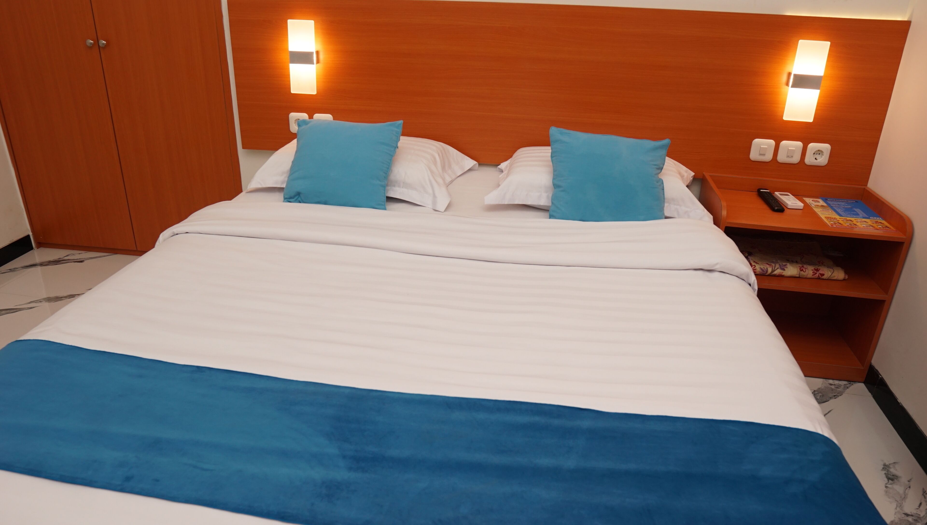 A hotel room with a bed, two pillows, a nightstand, and a wooden wardrobe.
