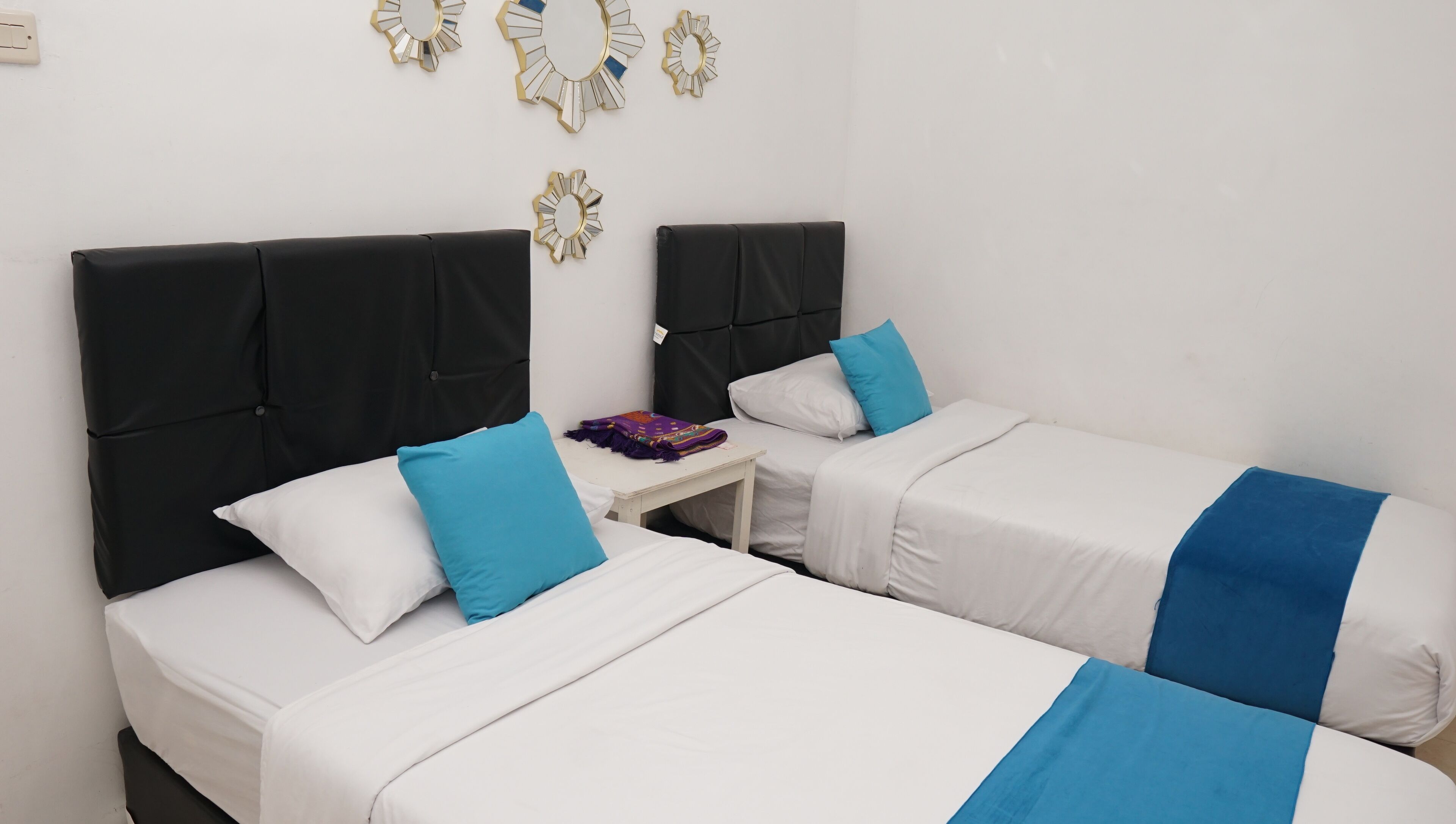 Two single beds with black headboards and white bedding, a small table with a purple blanket, and decorative wall mirrors.