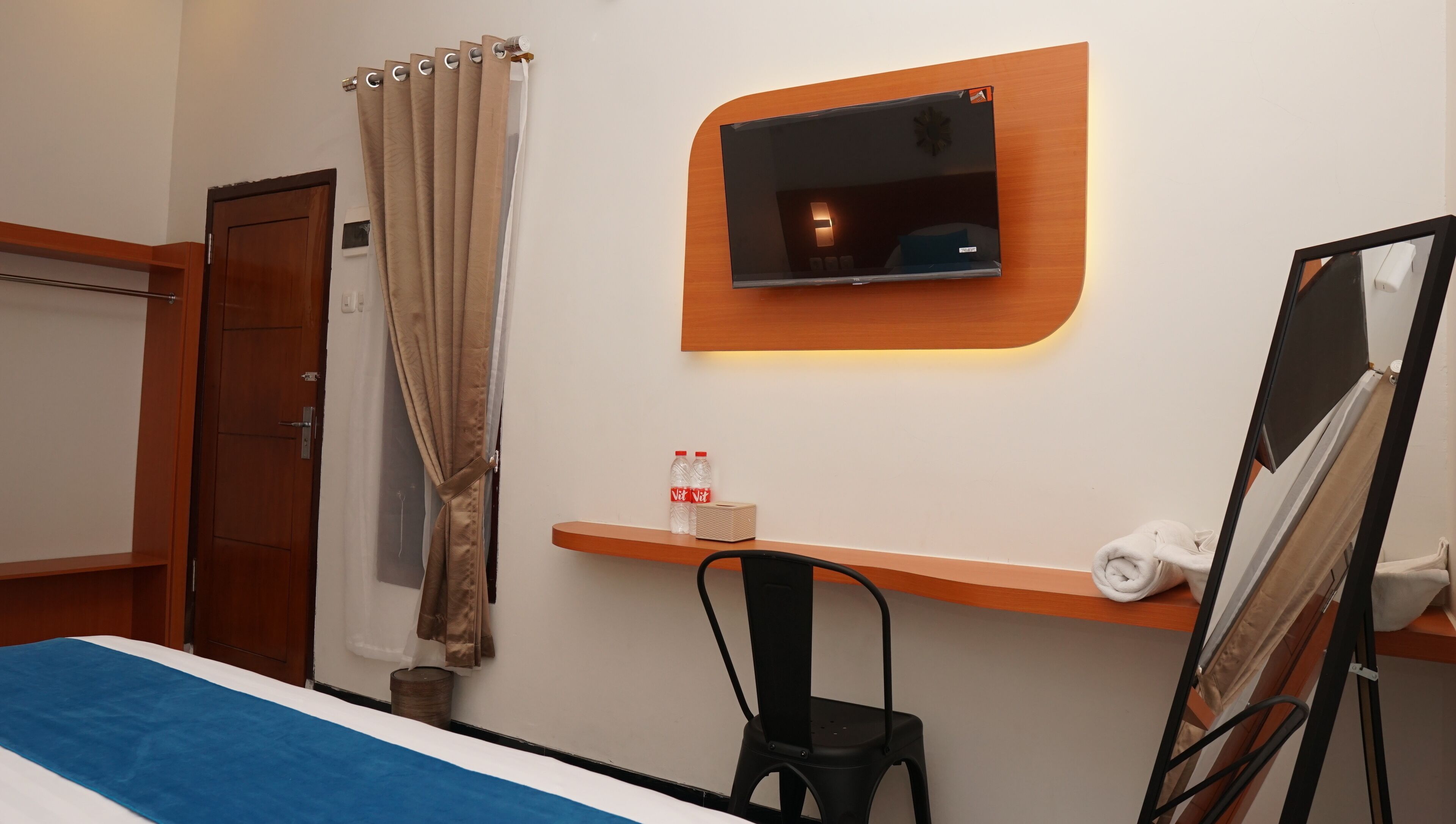 Une chambre d’hôtel comprenant un lit, un bureau avec un écran d’ordinateur, une chaise, une petite table avec des articles de toilette et un rideau.