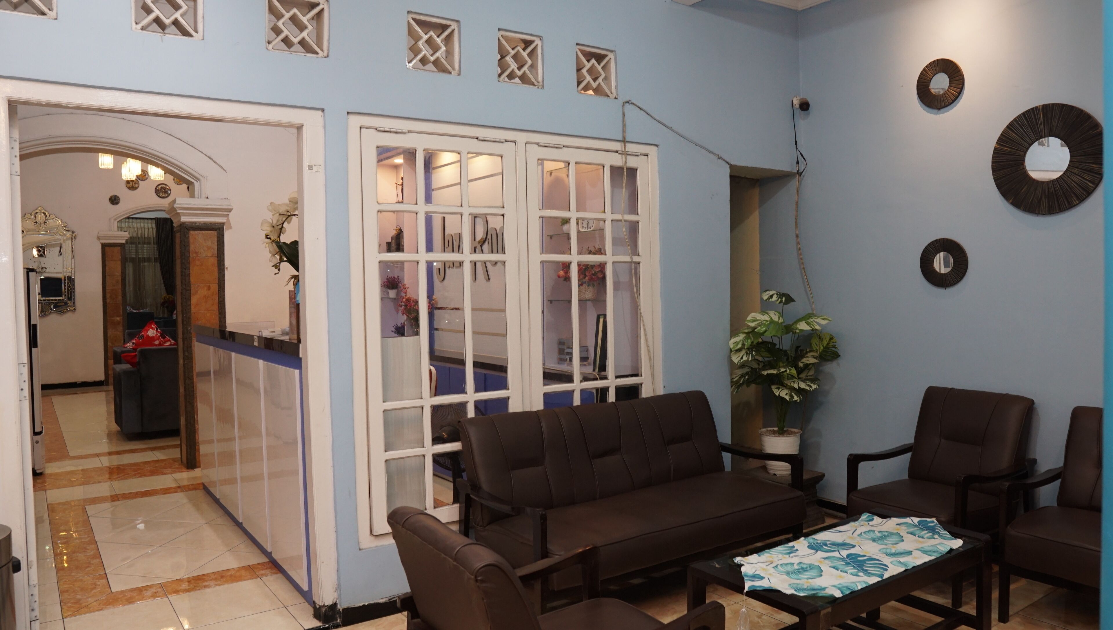 A living room with a brown sofa set, a coffee table, and a potted plant. There is a door leading to another room with a mirror and a small table.