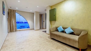 Un vaste espace de vie comprenant un canapé beige, une grande fenêtre avec des rideaux et un téléviseur vert fixé au mur.