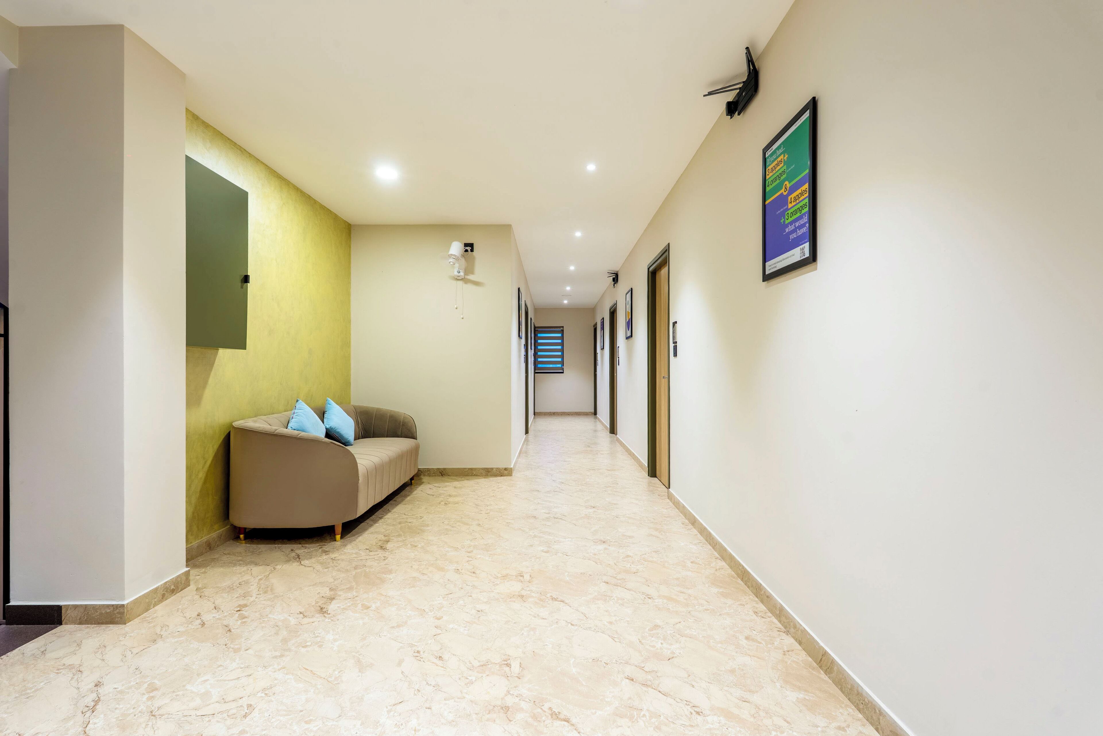 A hallway with a beige sofa, a yellow accent wall, and a framed poster on the wall.