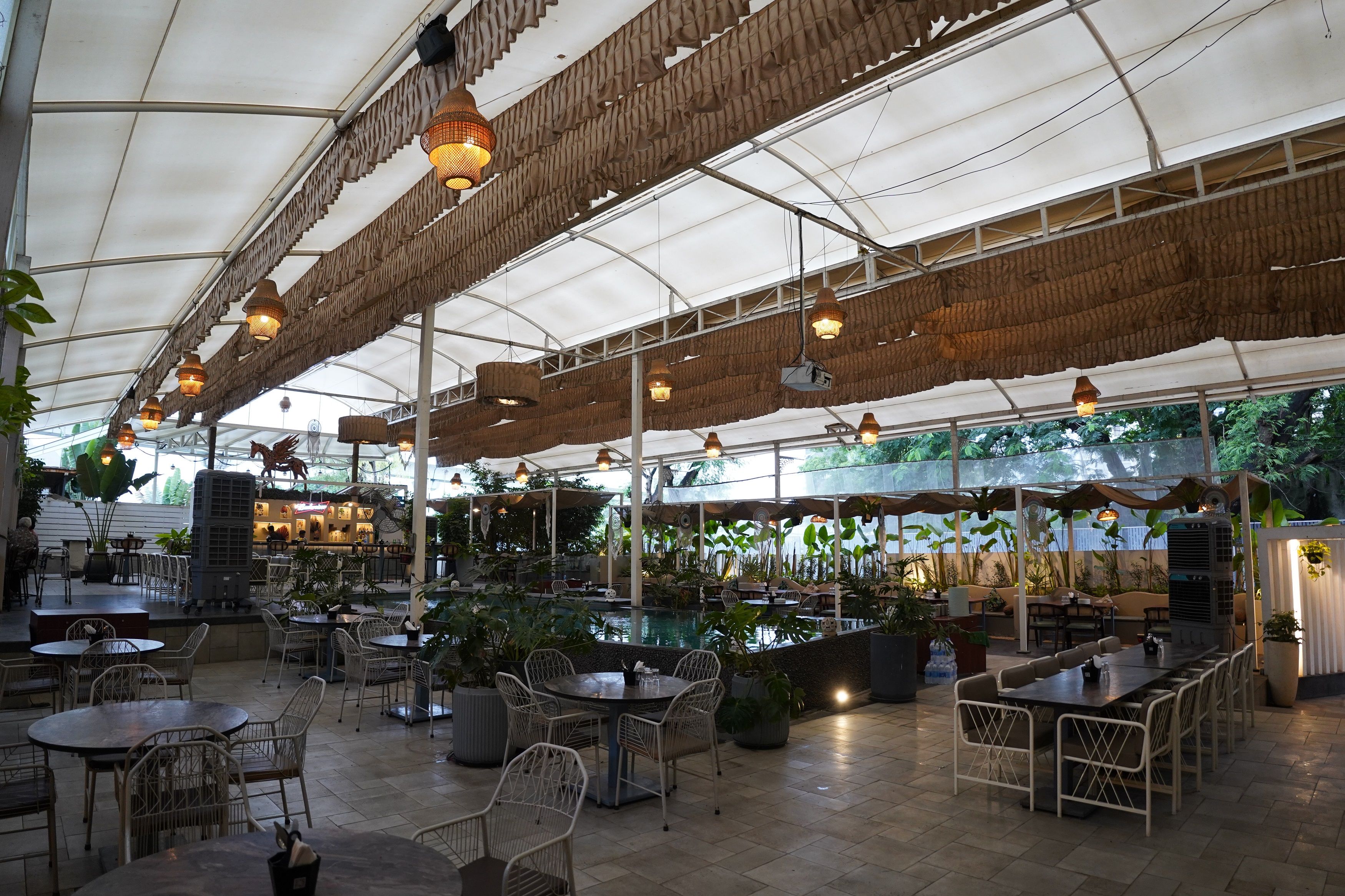 An indoor restaurant with high ceilings, hanging lights, and a variety of seating arrangements including tables and chairs.