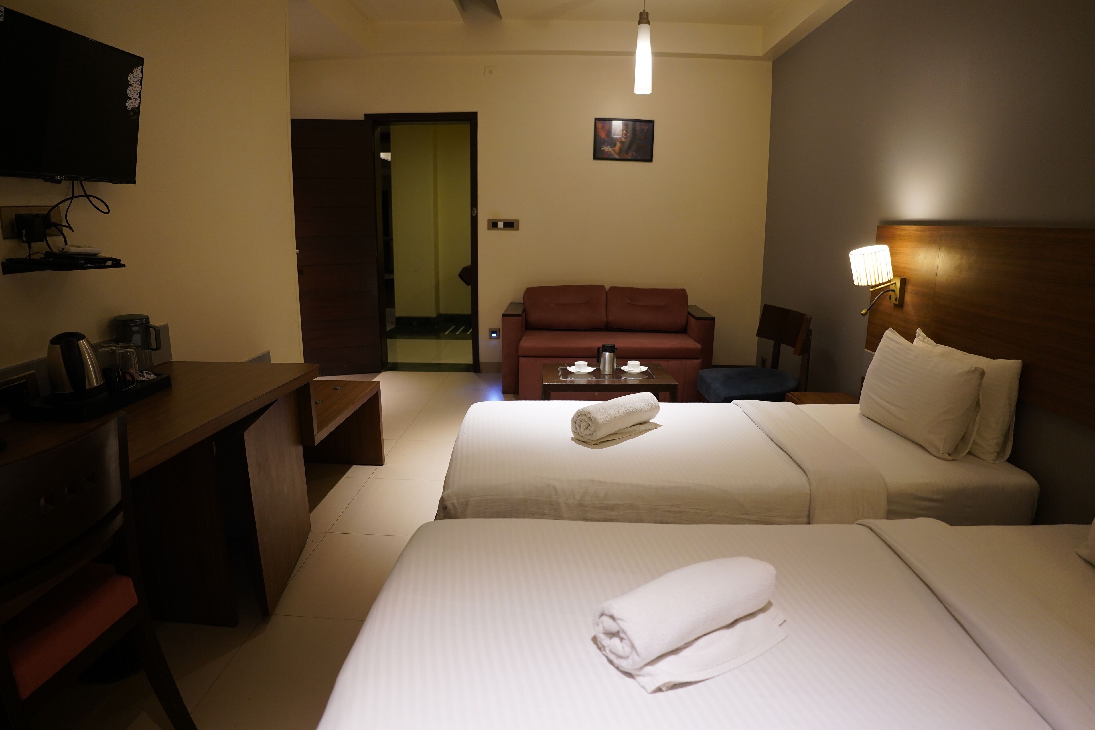 Een hotelkamer met twee bedden, een bureau, een koffiezetapparaat, een televisie en een bank.