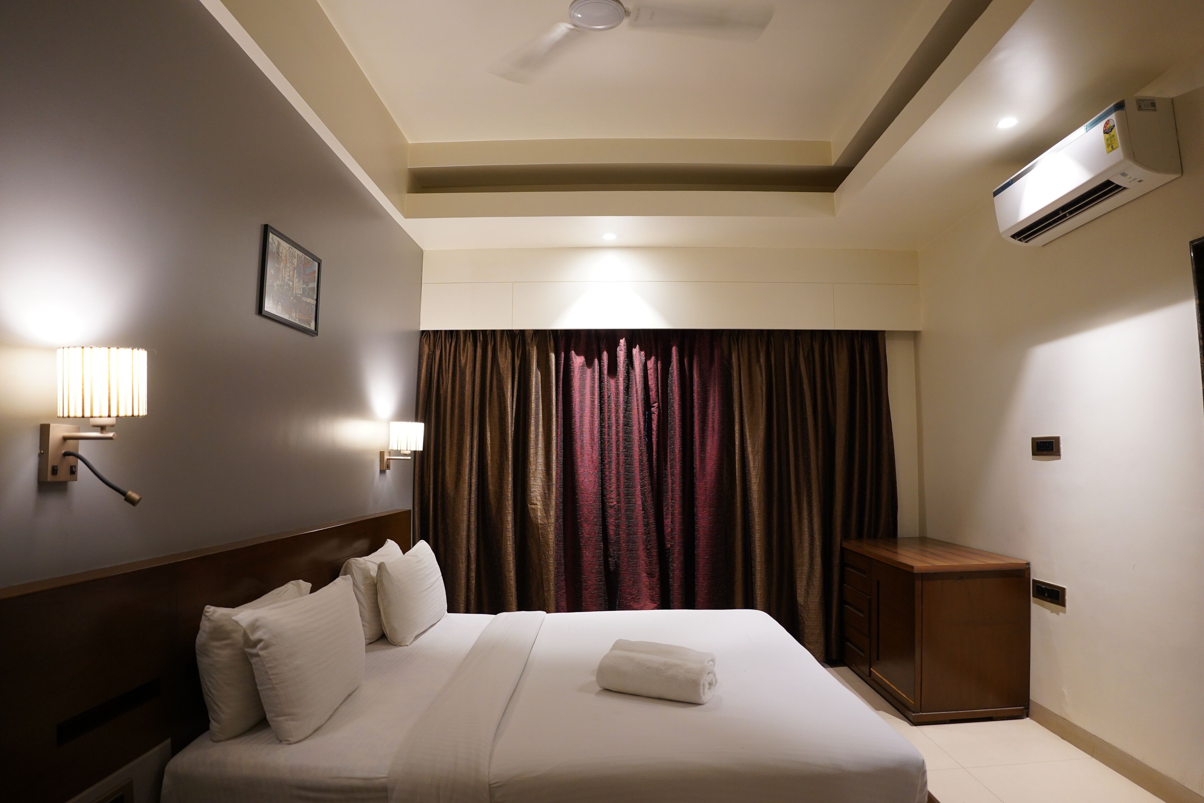 A hotel room with a bed, bedside lamps, an air conditioner, and a curtain.