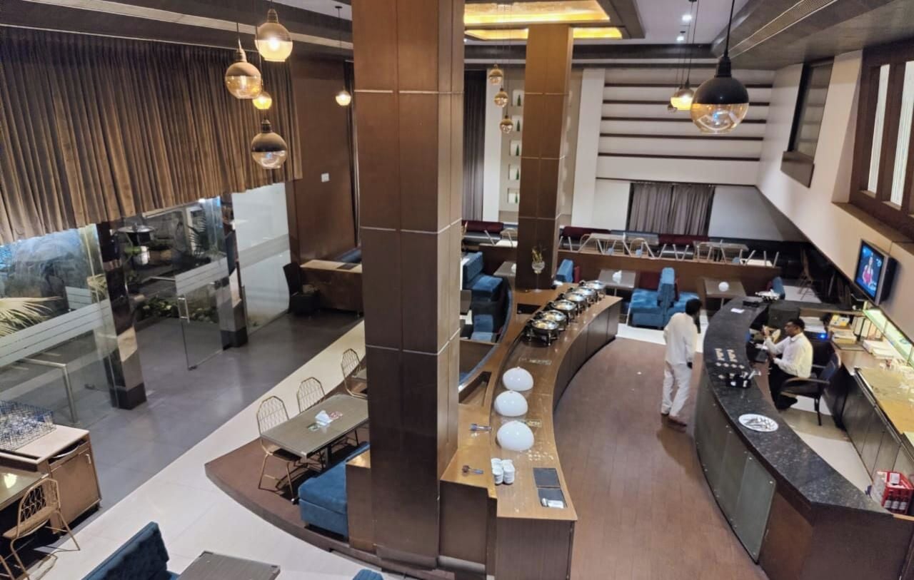 Um lobby de hotel moderno com área de estar central, balcão de recepção e uma grande janela com vista para o interior.