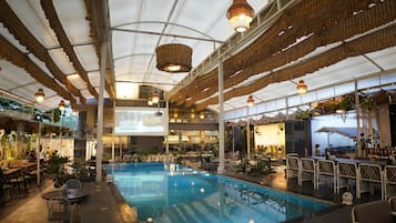 An indoor swimming pool with a ceiling that has a unique woven design, surrounded by tables and chairs.