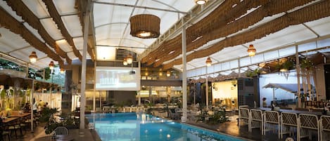 Una piscina interior con techo de diseño trenzado único, rodeada de mesas y sillas.