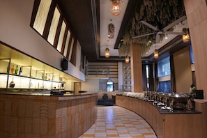 A modern bar area with a curved counter, hanging lights, and a ceiling with a fan and greenery. - Hotel Sadanand Regency - Balewadi, Baner (Paud)