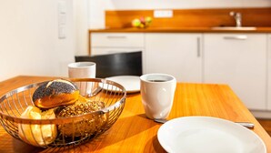 Un esmorzar amb una cistella metàl·lica que conté pa, una tassa blanca i un plat sobre una taula de fusta.