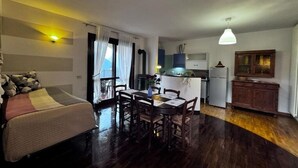 Quarto compacto com cama, mesa de jantar com cadeiras, cozinha compacta e varanda com cortinas.