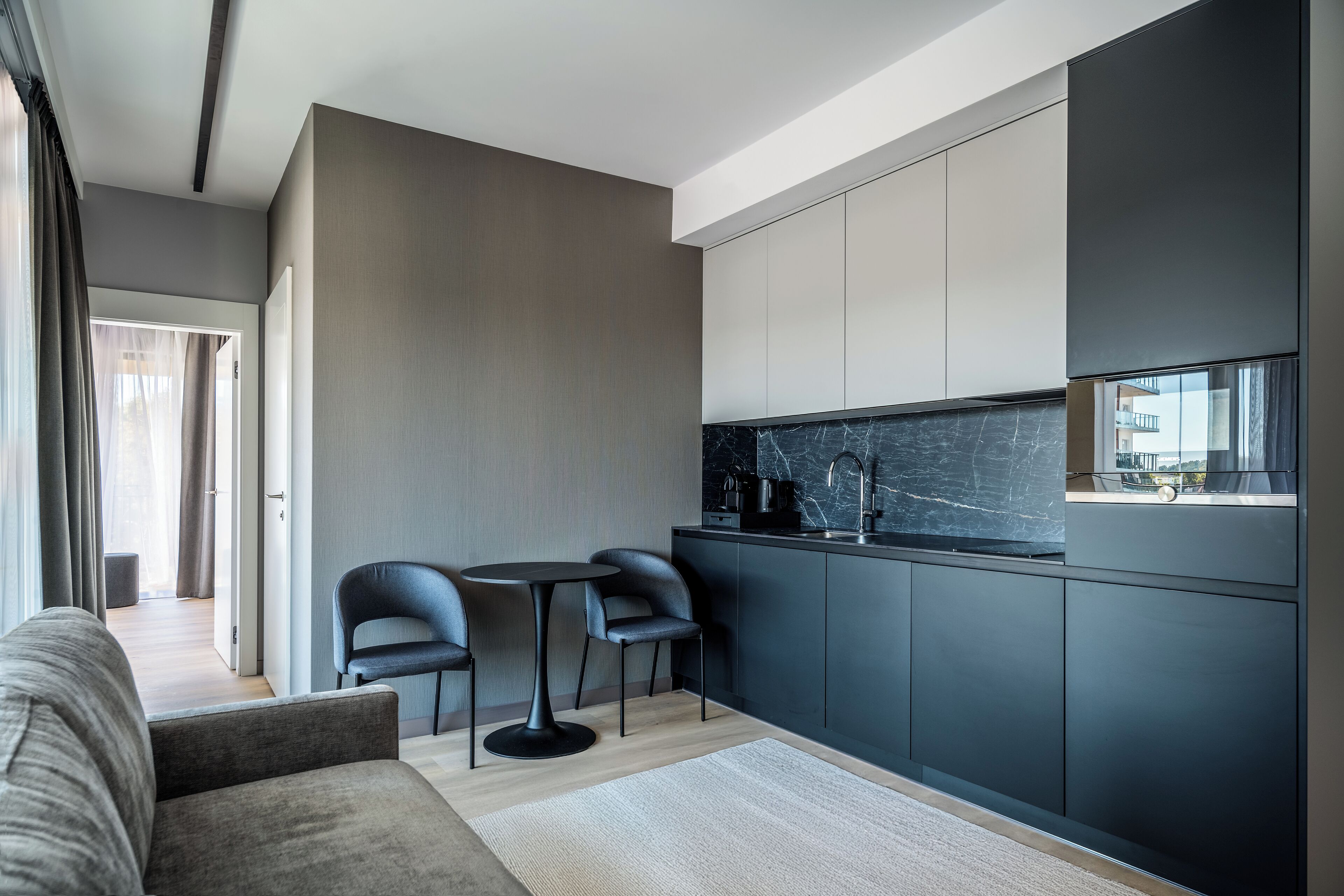 A modern kitchen with dark cabinets, a marble countertop, and a small dining area with two chairs and a table.