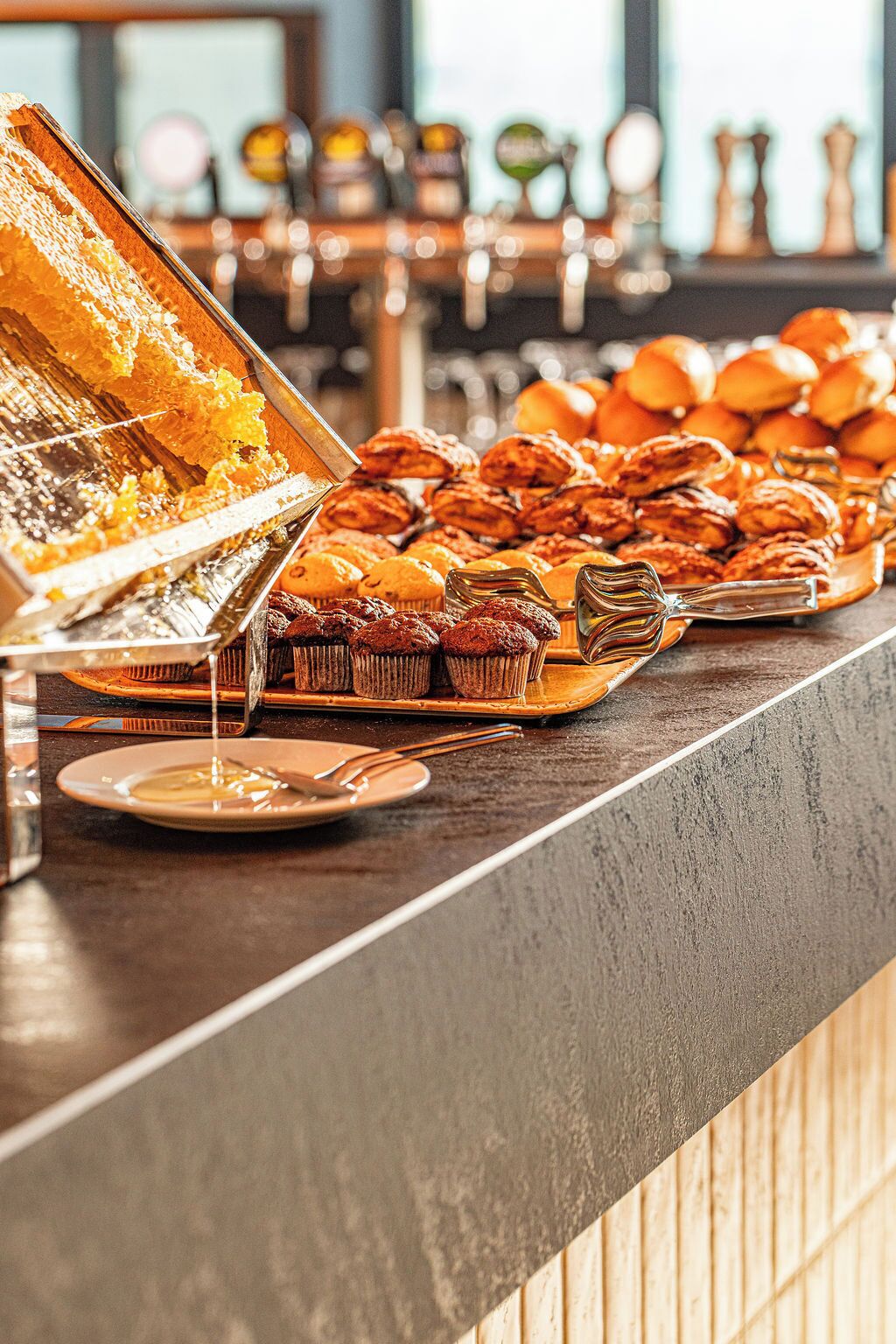 A buffet with various baked goods and a honey dispenser.