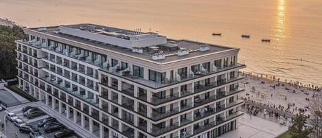 A multi-story building with a rooftop terrace, adjacent to a waterfront promenade.