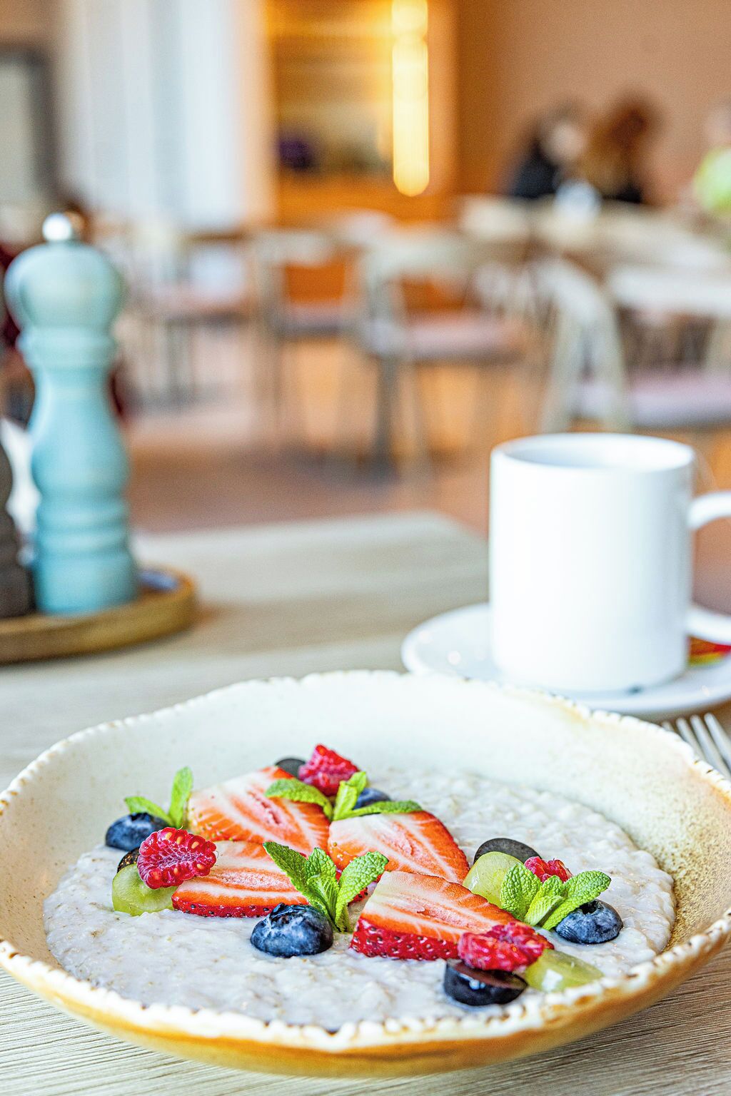 A dessert with fruit on a plate, a white cup, and a blurred background of a dining area.