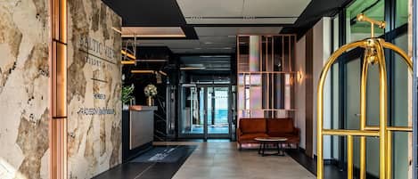 A modern hotel lobby with a reception desk, a sofa, and a golden gate.