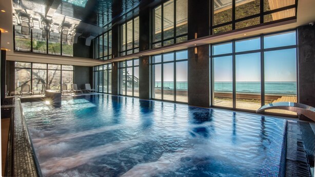 A large indoor swimming pool with a view of the beach through large windows. - Baltic View Resort & Spa, A Member Of Radisson Individuals (Miedzyzdroje)