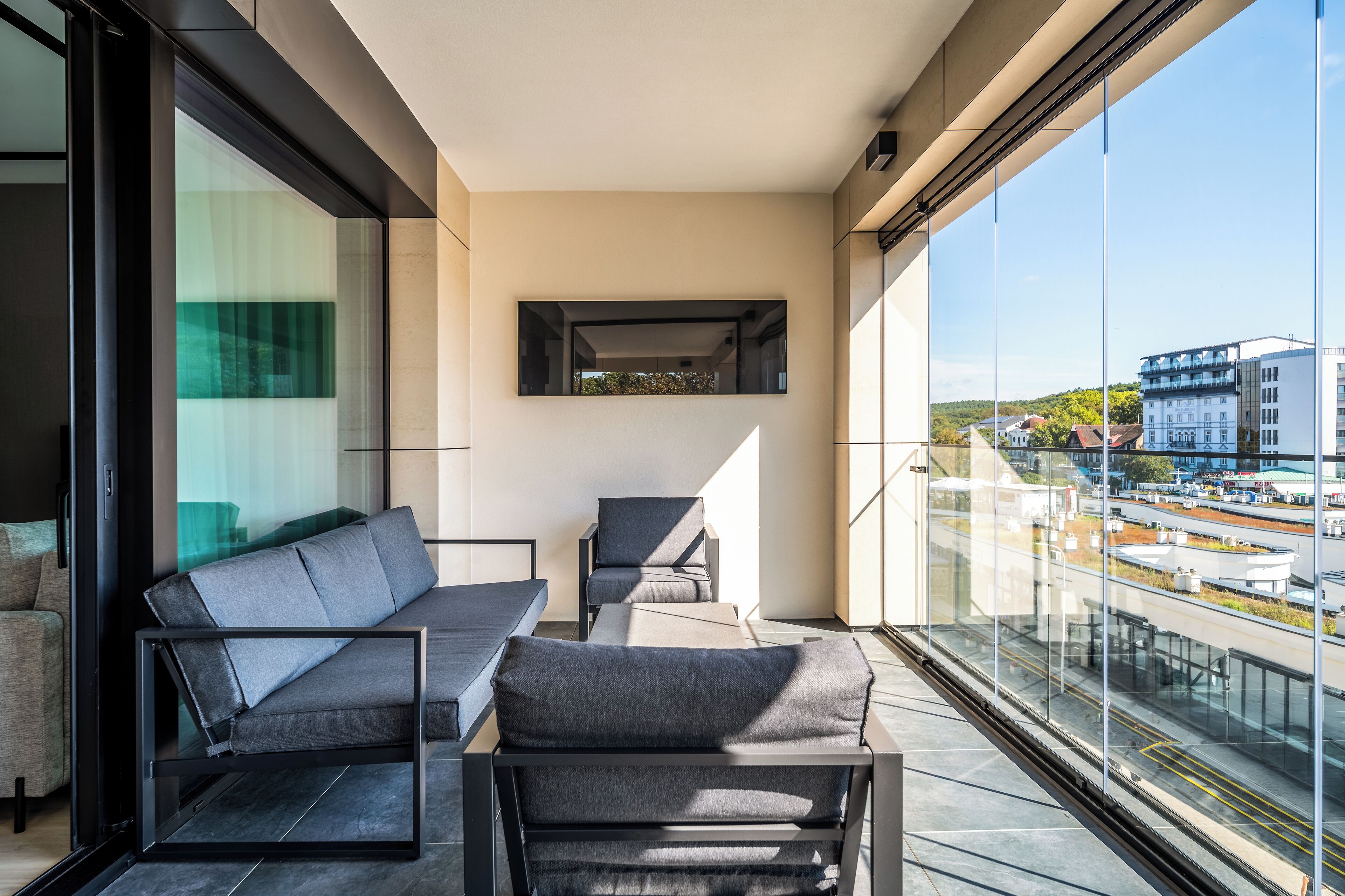 Un balcón moderno con sofá, sillas y una mesa, con vistas a un paisaje urbano.