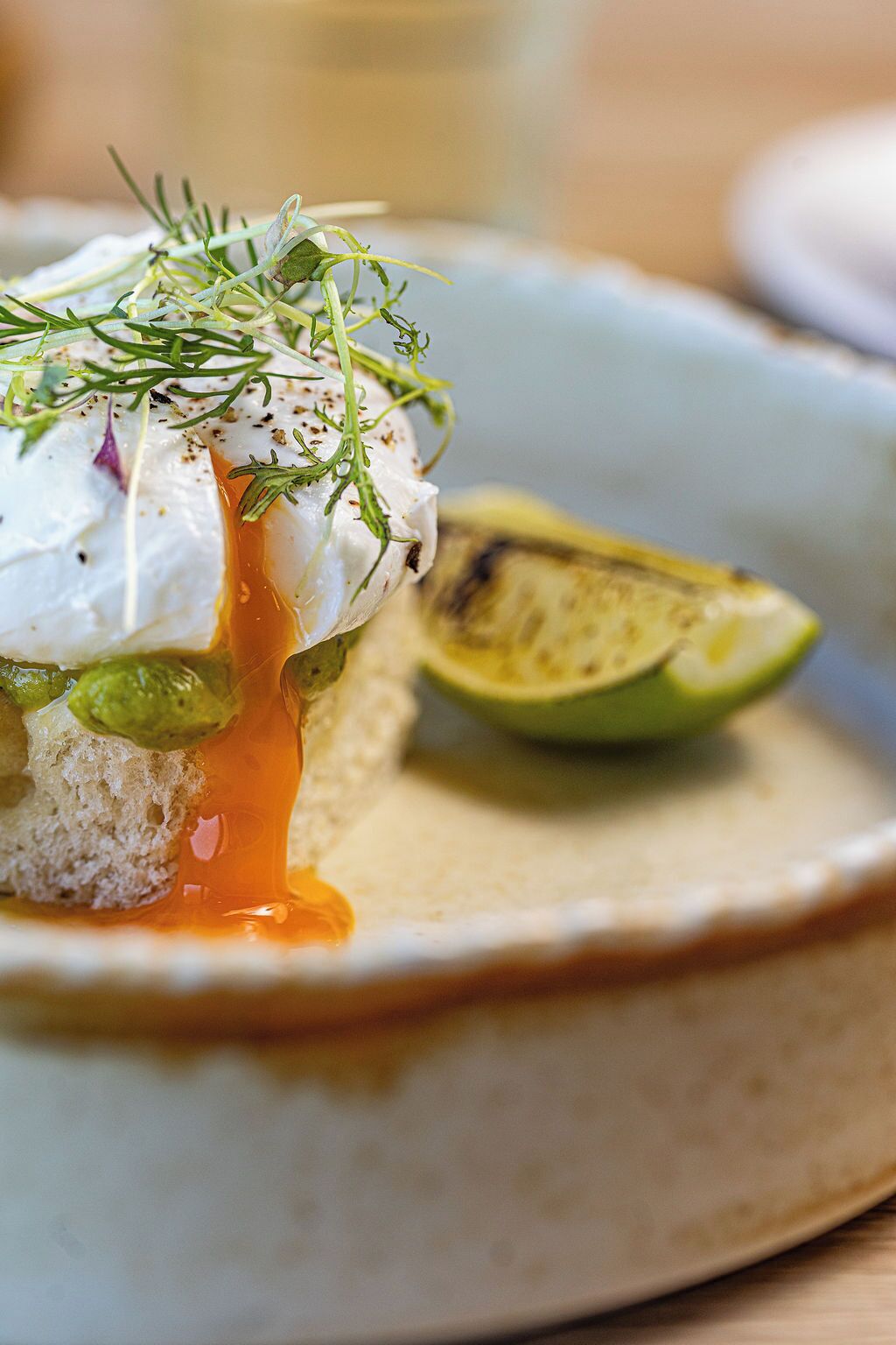Une assiette avec un œuf poché, de l’avocat et une tranche de citron vert.