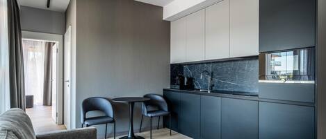 A modern kitchen with dark cabinetry, a marble countertop, and a small dining area with two chairs and a table.