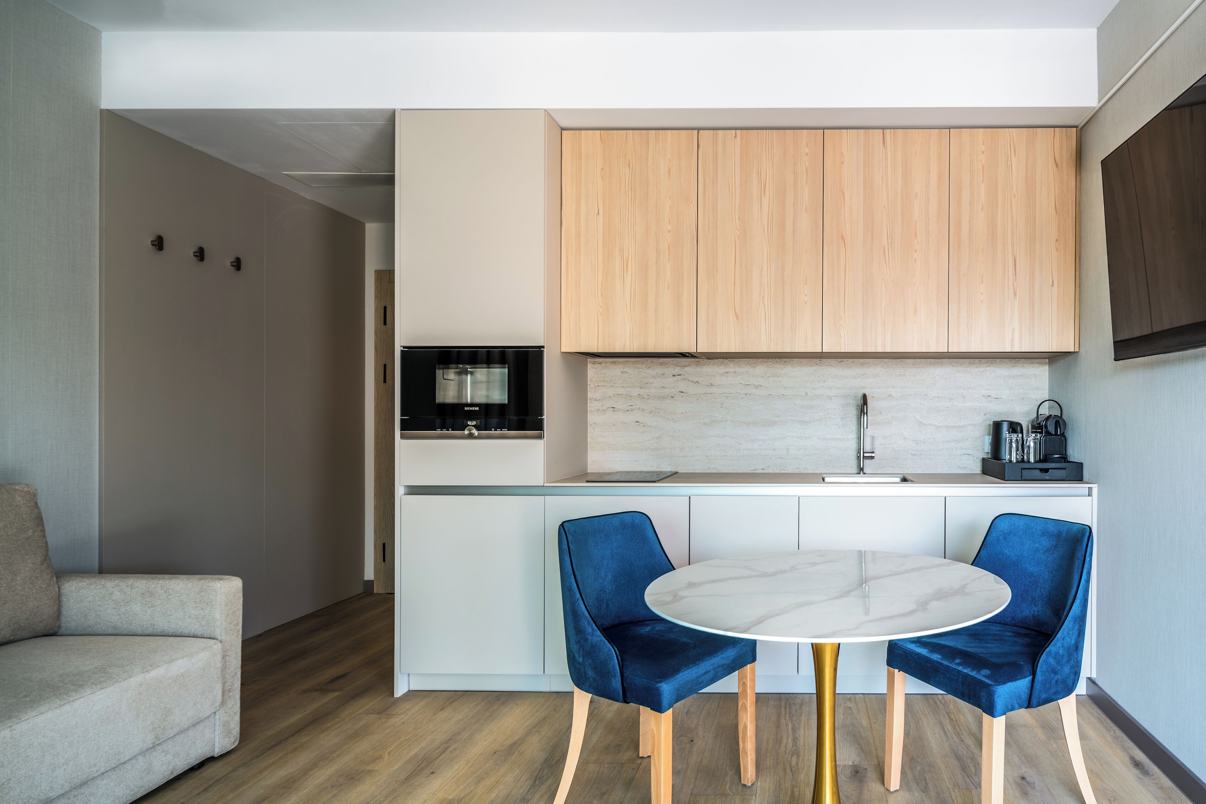 Una cocina compacta con armarios de madera, una encimera blanca y una mesa redonda de mármol con dos sillas azules.