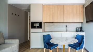 Una cocina compacta con armarios de madera, una encimera blanca y una mesa redonda de mármol con dos sillas azules.