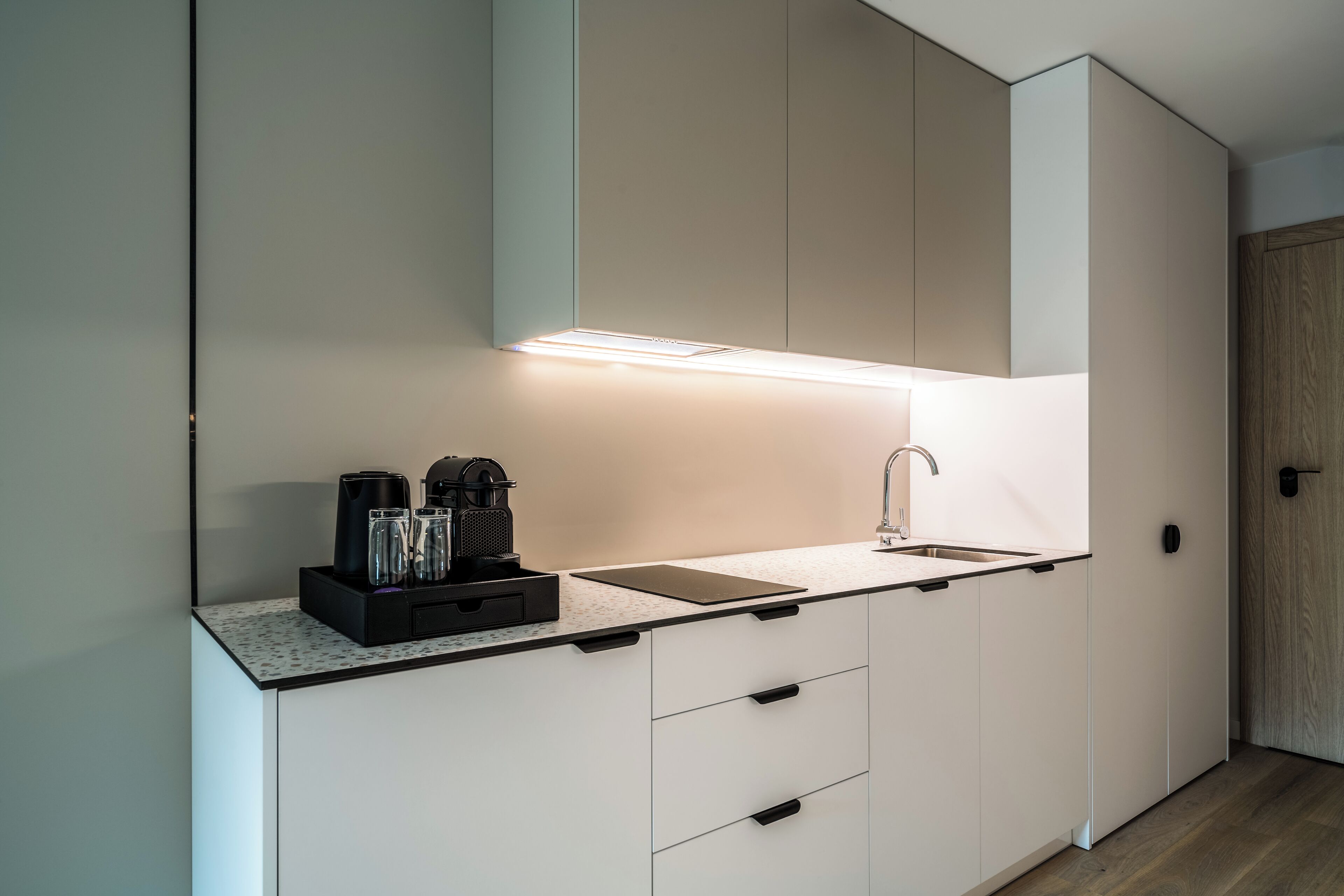 A modern kitchen with white cabinetry, a countertop, a coffee maker, and a sink.