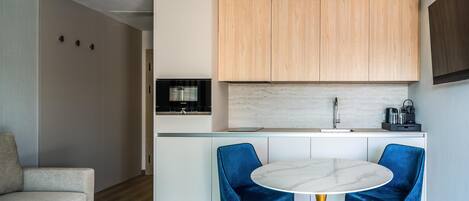 Una cocina moderna con armarios de madera, encimera blanca y una mesa de mármol con dos sillas azules.