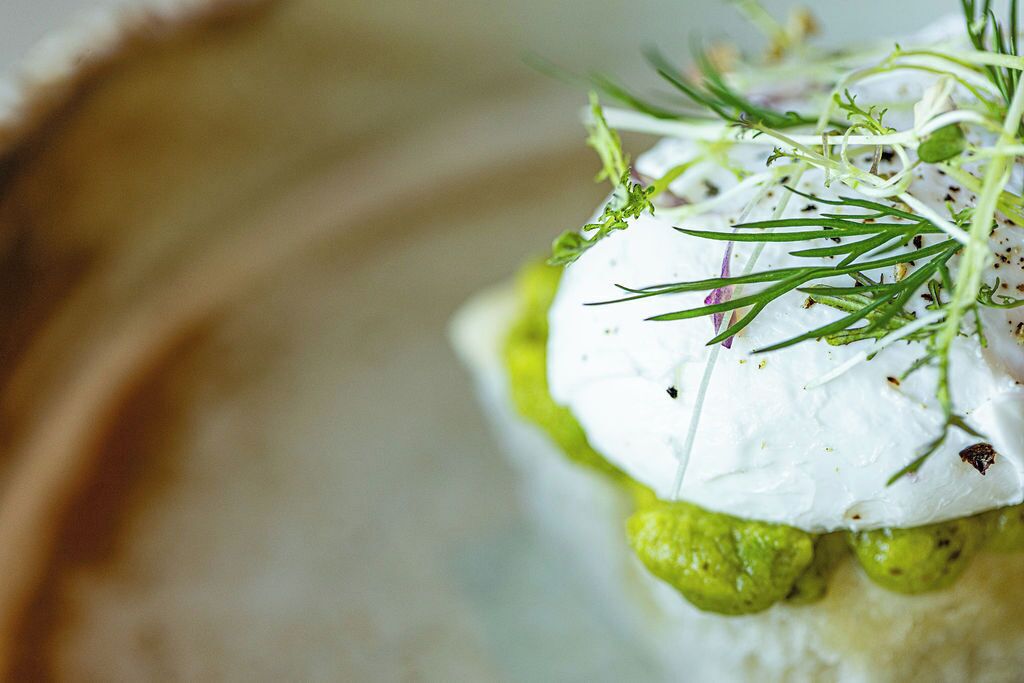 Close-up van een bord met een romige witte topping, groene saus en verse kruiden.