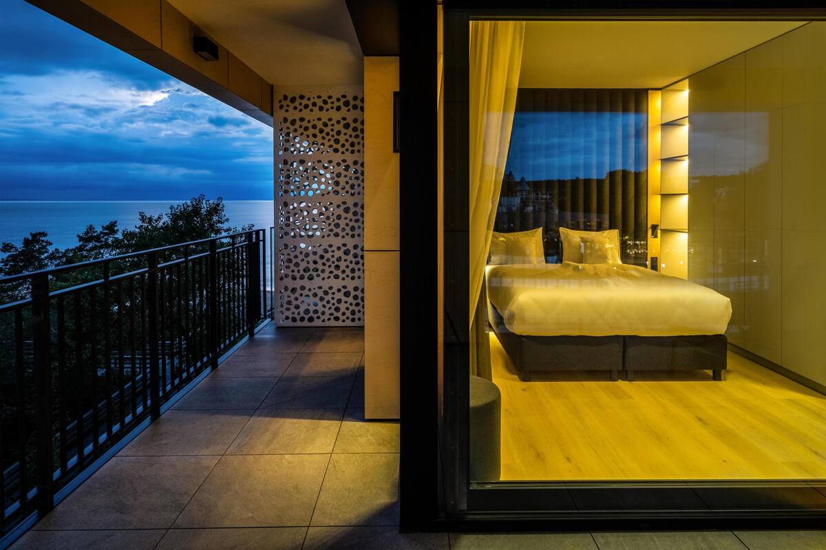 Une chambre moderne avec un grand lit, une vue sur la mer et un balcon doté d’une balustrade.