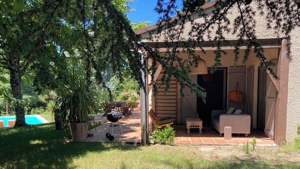 Un espace extérieur abrité, aménagé avec une table et des chaises, un barbecue et une petite table en bois.