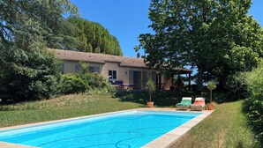 Une piscine rectangulaire, bordée d’une terrasse carrelée et entourée de pelouse et d’arbres.