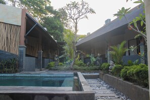 Une cour intérieure avec une piscine, entourée de bâtiments modernes aux façades en bois et aux éléments décoratifs en pierre.