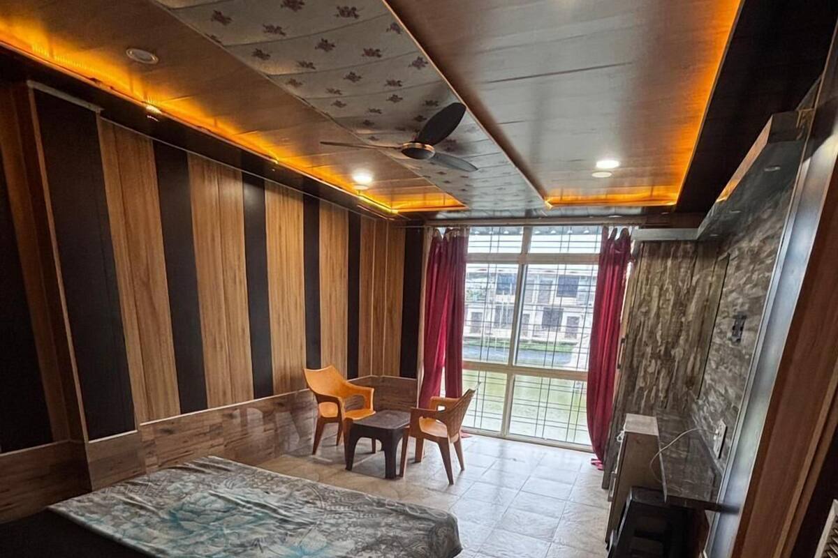 Ett hotellrum med en säng, en liten sittgrupp med stolar, en takfläkt och utsikt genom ett stort fönster.