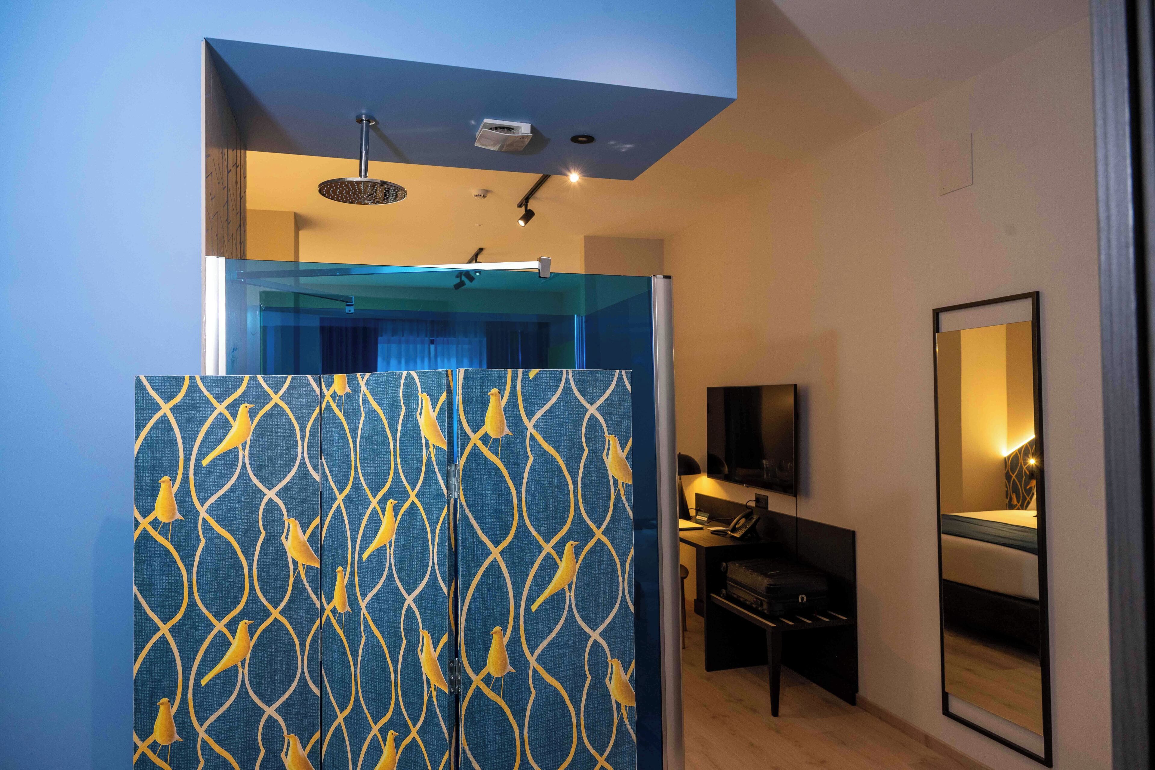 Una habitación de hotel moderna con zona de ducha, un escritorio con silla y un televisor montado en la pared.