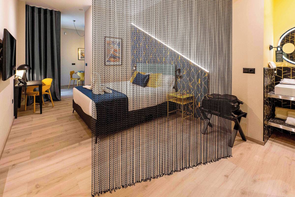 A modern hotel room with a bed, a desk, a chair, and a bathroom area.