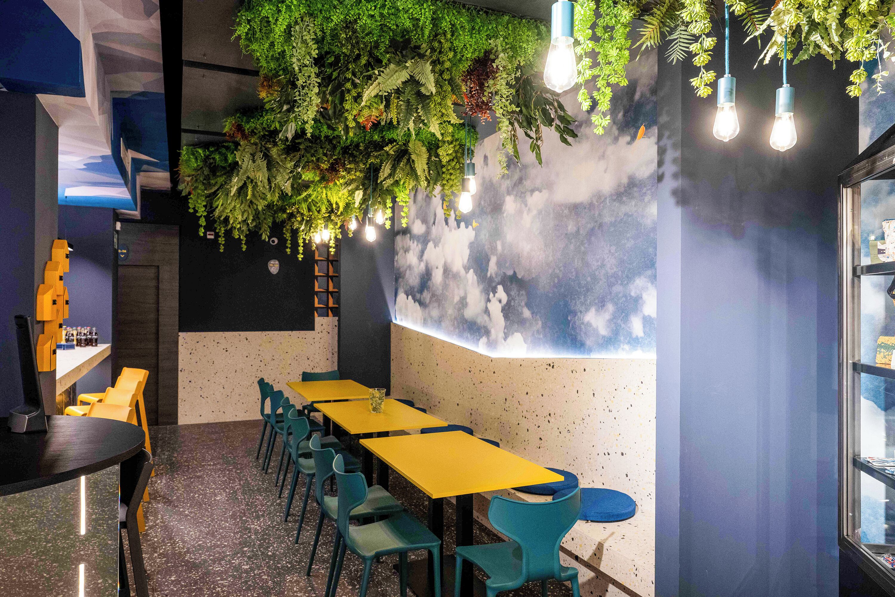 A restaurant with a long table, chairs, and hanging plants.