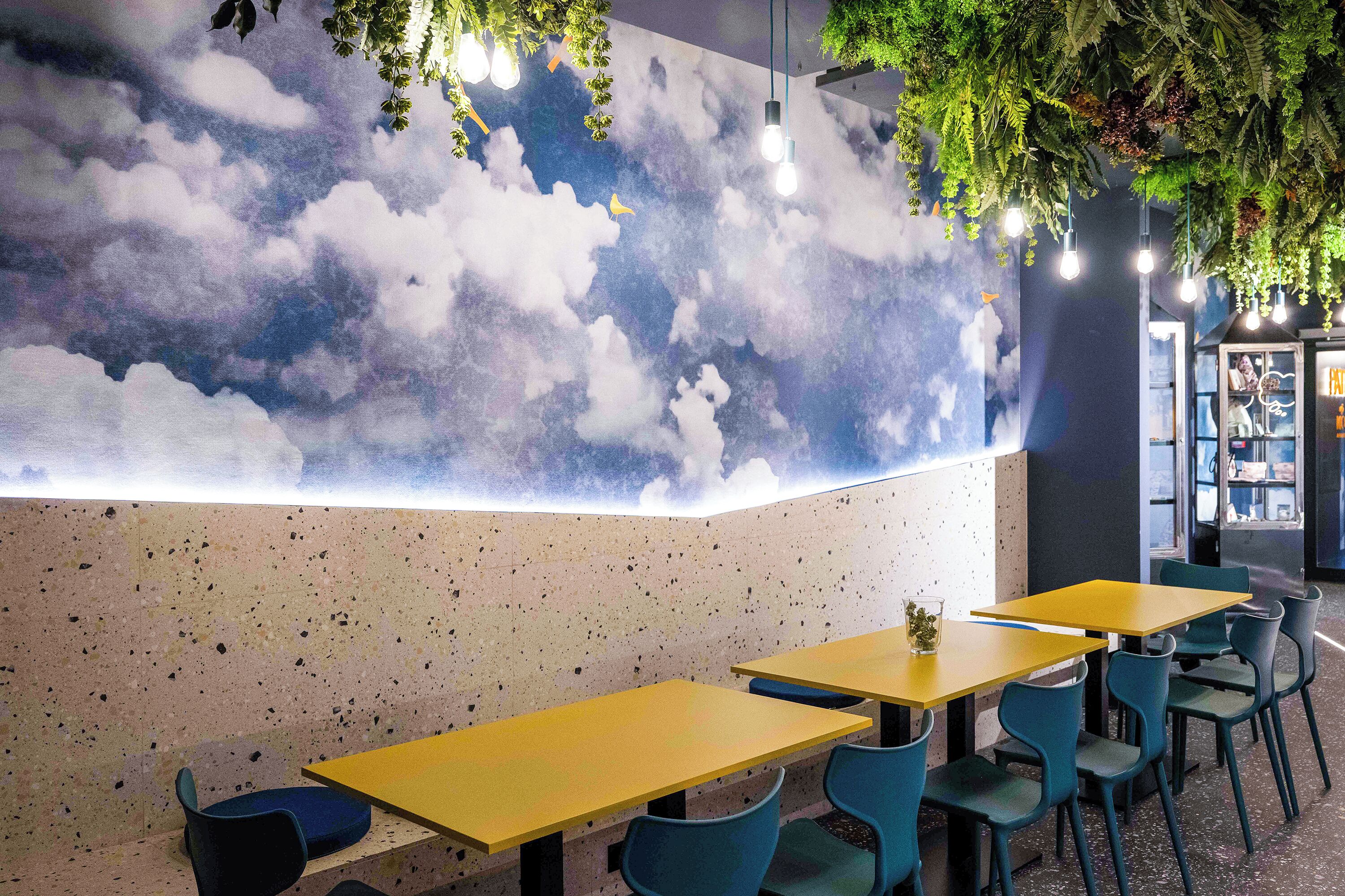 A restaurant with a cloud-themed wall, tables, and chairs.