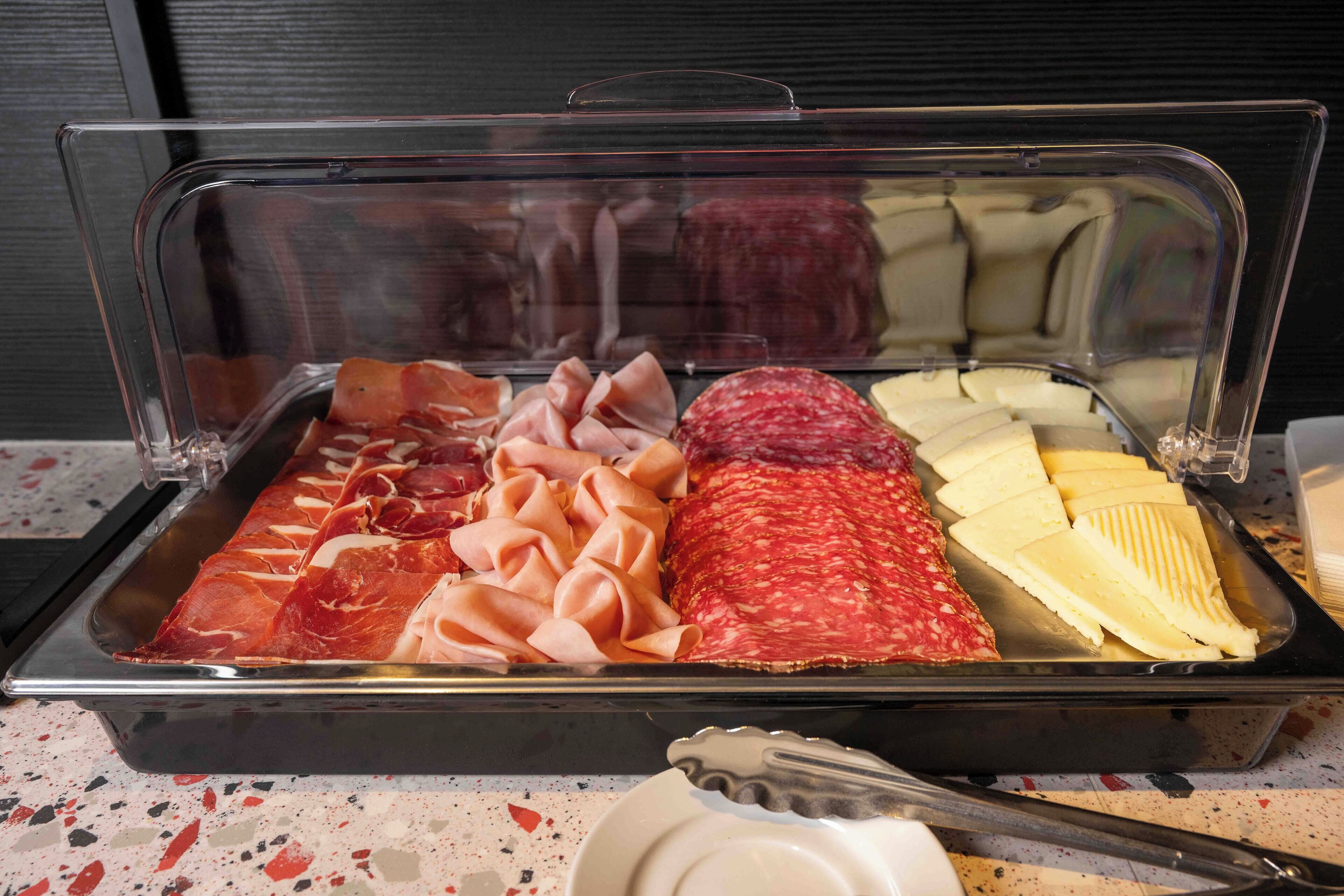 Un bufé con varias carnes y quesos, incluyendo prosciutto, salami y queso en rebanadas.