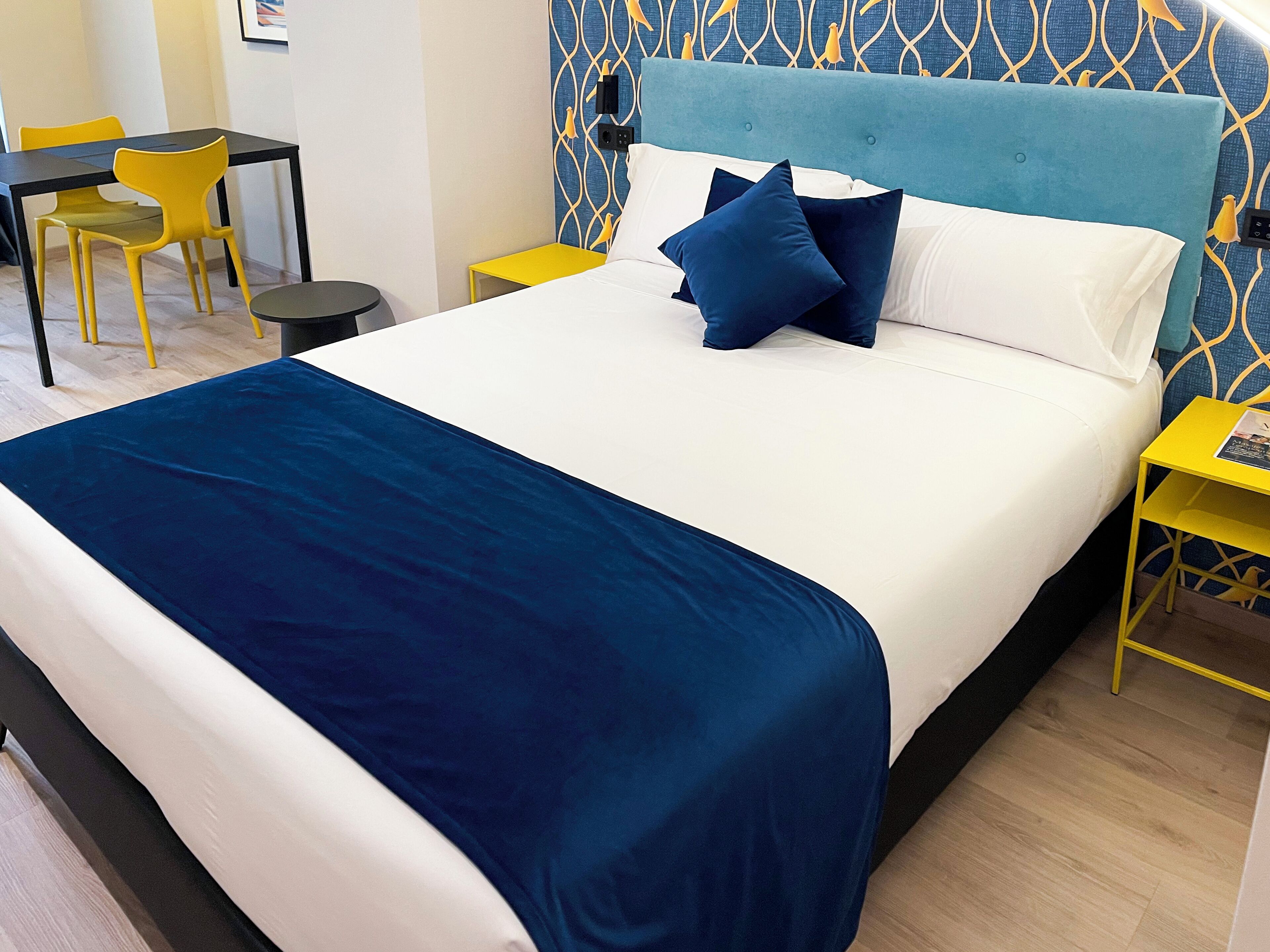 Una habitación de hotel con una cama grande, una mesita de noche, una silla y una pequeña mesa con lámpara.
