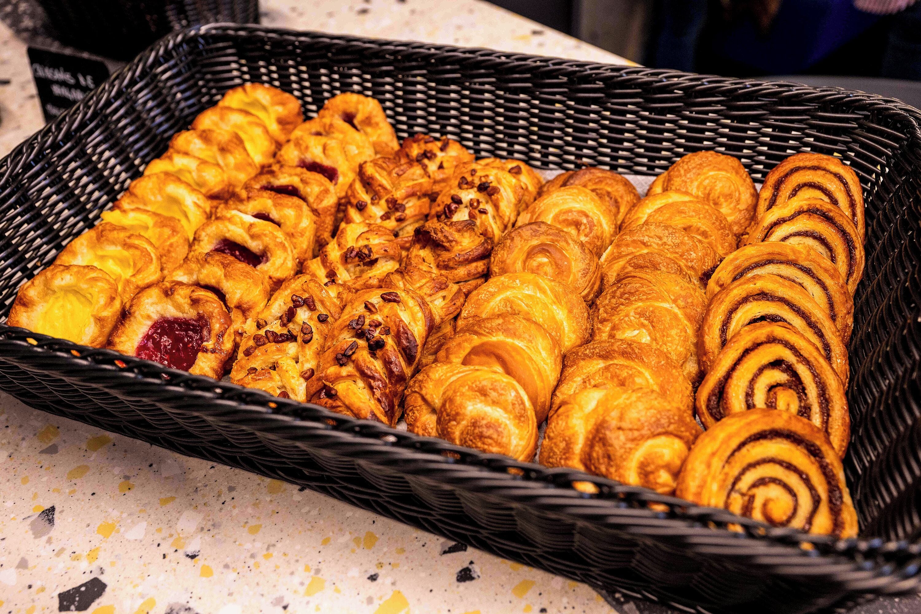 A basket filled with various pastries, including croissants and cinnamon rolls.