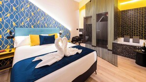 Une chambre d’hôtel avec un grand lit, une tête de lit ornée d’un motif bleu et jaune, un mur au décor géométrique et une cloison aux motifs noir et blanc.